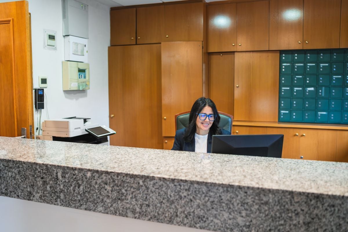 Smiling receptionist woman working on computer at an office desk, providing professional service in a modern nursing home setting